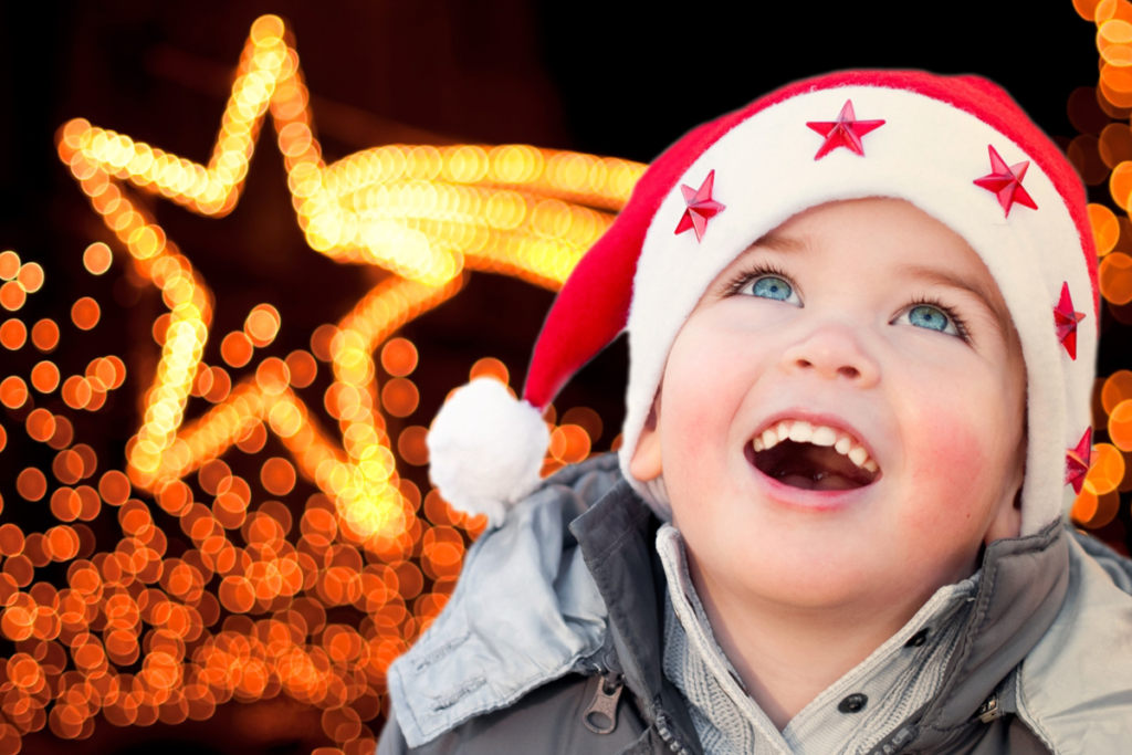 Een kindje dat verwonderd naar boven kijkt, met een kerstmuts op en een lichtgevende ster achter hem.