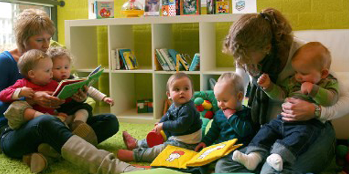 Twee vrouwen met babies op schoot lezen voor uit boekjes