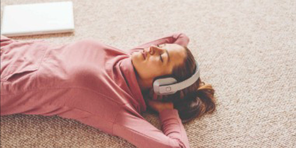 Vrouw ontspannend liggend op de grond met koptelefoon op - Workshop Mindfulness